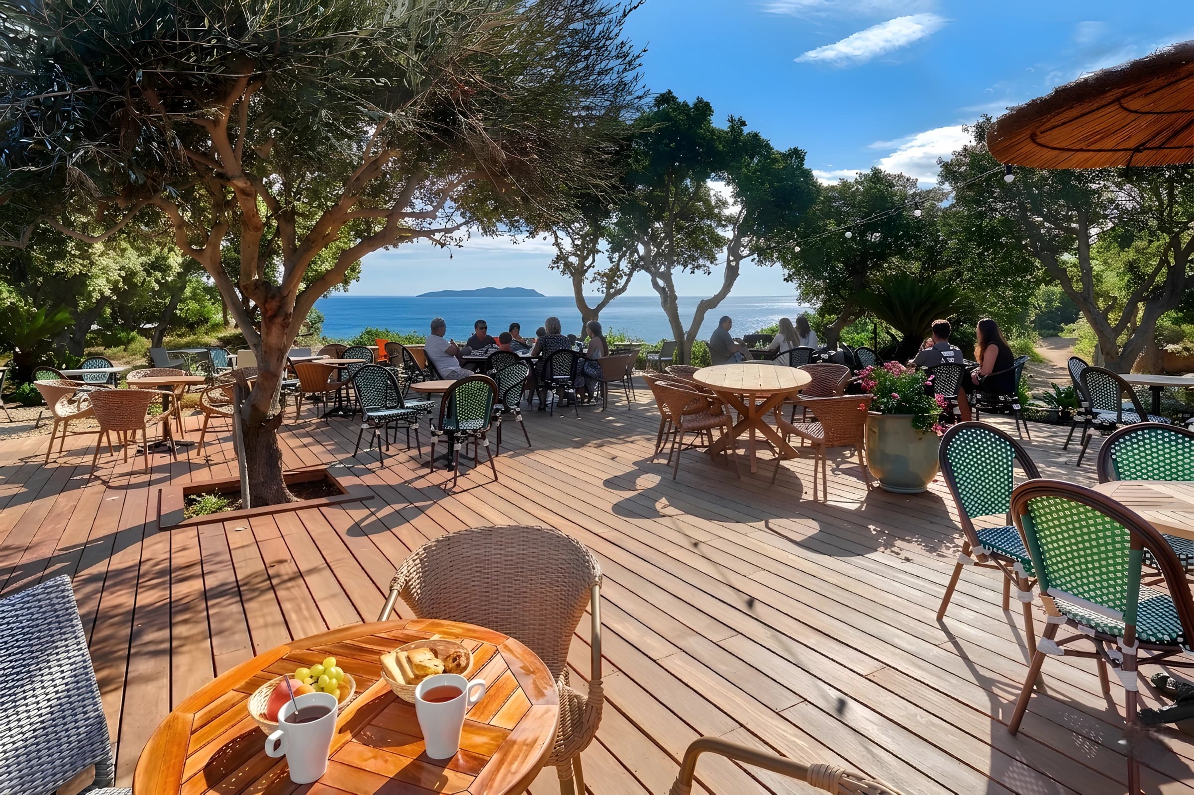 Terrasse en bois de L'Azéa avec parasols de paille, oliviers et vue sur la mer Méditerranée